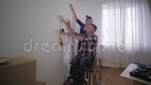 家庭友好年轻美丽的妻子和幸福的丈夫残疾人在轮椅上选择壁纸在修理期间视频的预览图