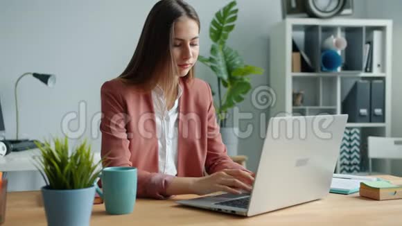 一幅美丽的女商人带着笔记本电脑坐在办公桌前微笑的画像视频的预览图