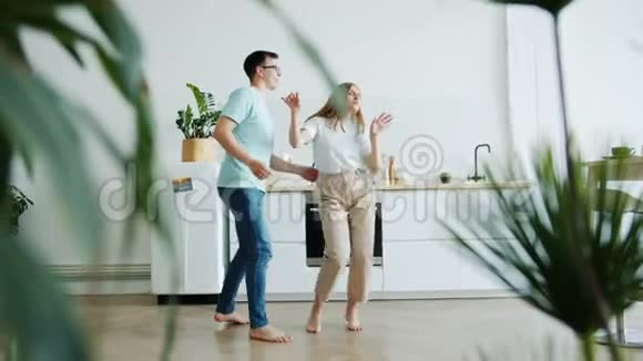 慢动作的年轻夫妇在家里的厨房里跳舞手牵手玩得开心视频的预览图