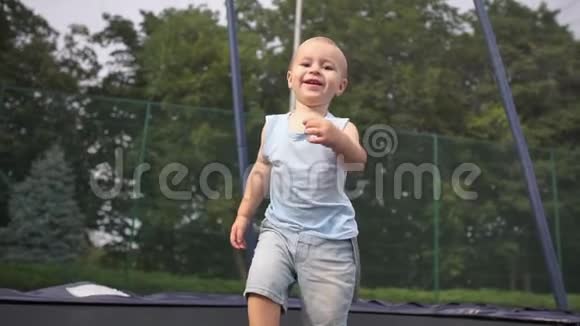 可爱的微笑婴儿蹦蹦跳跳并落入一个坐在蹦床上的位置视频的预览图