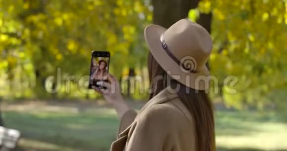 年轻的高加索女孩穿着优雅的衣服在公园的智能手机上自拍漂亮的欧洲女人周末视频的预览图