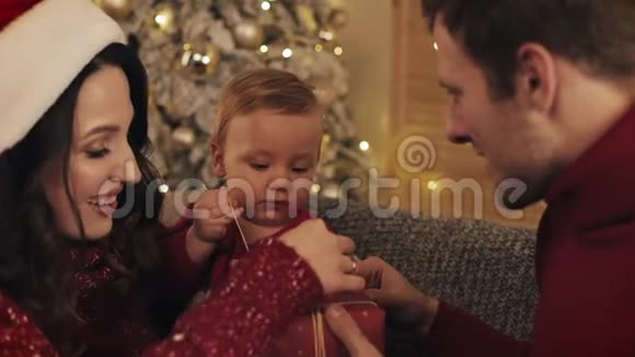 亲近快乐的白种人父母帮助他们的孩子打开礼物盒穿在冬天的毛衣坐在舒适视频的预览图