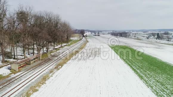 一场雪后沿阿米什农场土地的蒸汽机和乘用车的鸟瞰图视频的预览图
