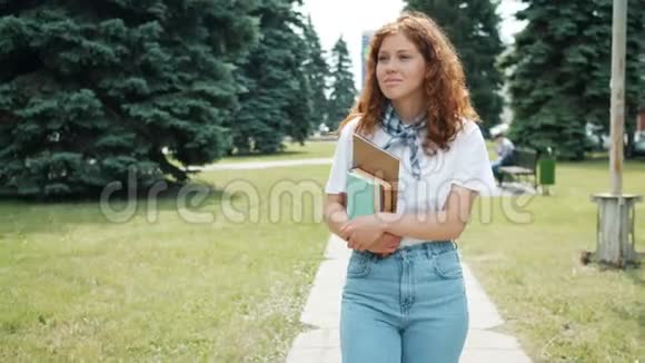 秋天一个红发女学生在公园里散步手里拿着书微笑着视频的预览图