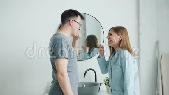 穿着睡衣的男人和女人刷牙在现代公寓里微笑着说话视频的预览图