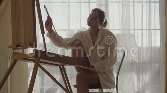 年轻女性白种人艺术家坐在她的房间里晒太阳和画画的肖像美丽的年轻女子画视频的预览图
