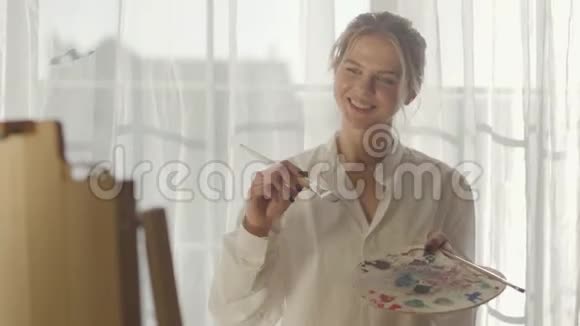 年轻的金发白种人女人站在她的卧室阳光下画画的肖像女性艺术家的绘画视频的预览图