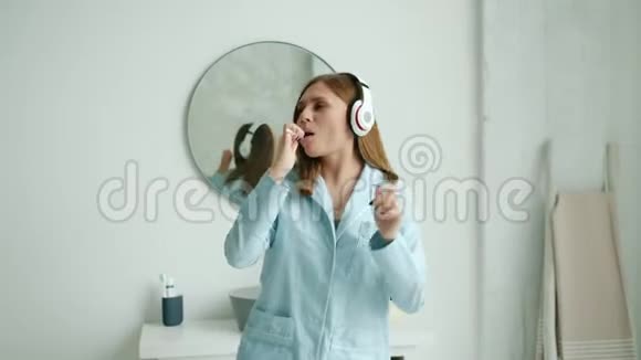 戴着耳机刷牙在浴室跳舞的快乐女人的慢动作视频的预览图