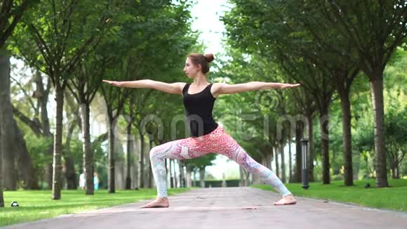 一个年轻的女孩站在公园小巷里慢动作的瑜伽姿势视频的预览图