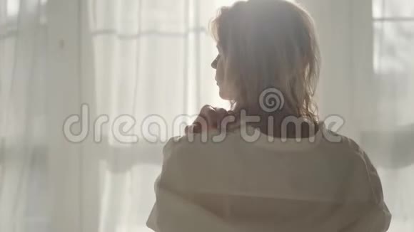 镜头移开金发白种人女孩穿着白色衬衫坐在床上迷人的年轻女子醒来视频的预览图