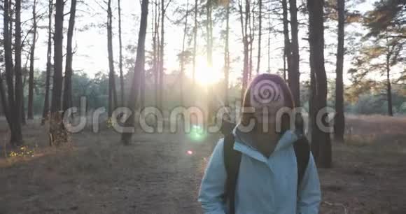 阳光明媚的秋日年轻微笑的快乐女人带着黑色的大背包在秋天的森林里散步女性旅行者享受阳光视频的预览图