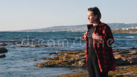 悲观的女人站在海边变得寒冷寂寞的女人在风秋天在海滩上结冰悲伤的女人看着大海视频的预览图
