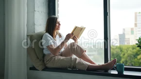 漂亮的女孩在家坐在窗台上翻书视频的预览图