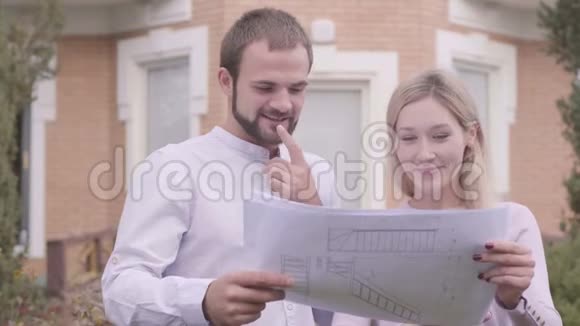 两个高加索人站在房子前面拿着蓝图说话专业建筑师视频的预览图