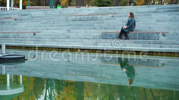 伤心的女孩坐在楼梯上在公园湖里沉思视频的预览图