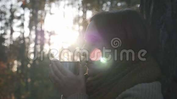 在秋天公园里年轻的黑发女人喝着热茶女性旅行者从大自然的热水瓶中喝咖啡视频的预览图