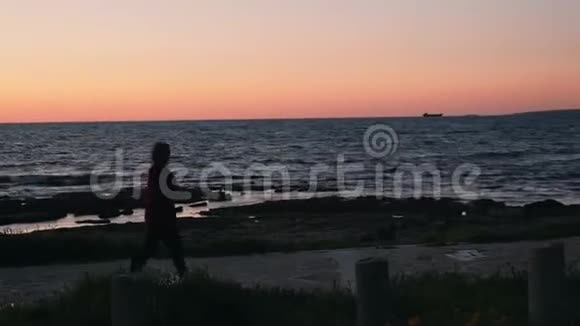 日落时分孤独的年轻女子沿着地中海海滨散步穿着保暖衣服的漂亮女人在沙滩漫步视频的预览图