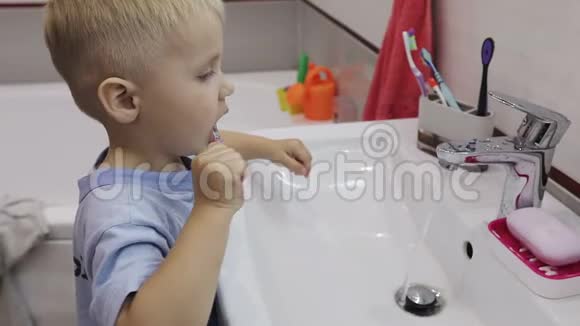一个穿蓝色t恤的小男孩在浴室的镜子前刷牙视频的预览图