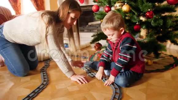 幸福的微笑母亲帮助她的儿子从克里斯塔姆斯树下的砖块建造铁路轨道的4K镜头儿童视频的预览图