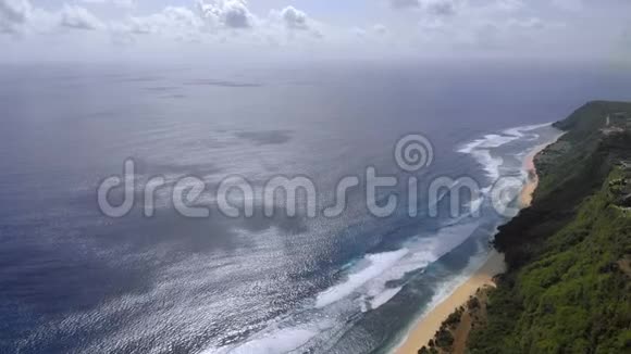 巴厘岛一片野生海滩的航拍照片一条长长的海滩和陡峭的山坡上覆盖着绿色植物视频的预览图