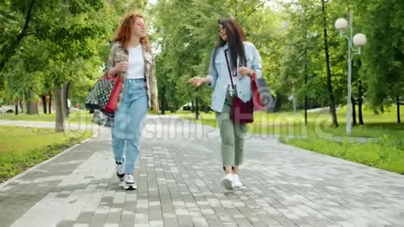 兴奋的朋友在公园散步时带着五颜六色的购物袋在那里做着击掌活动视频的预览图