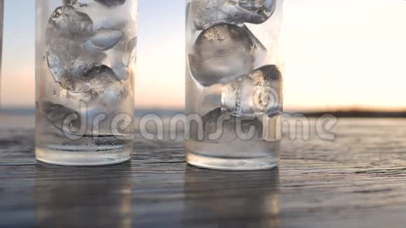 把水倒入一个清澈的玻璃杯里木桌上放着冰暮色中放着海滩视频的预览图