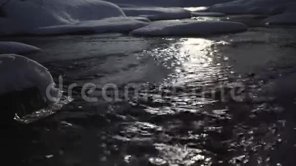 夜间射击快速移动的水经过雪岸月光反射在黑色的水中视频的预览图