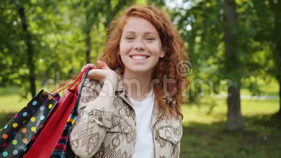 一个快乐的女孩带着购物袋独自站在公园里微笑视频的预览图