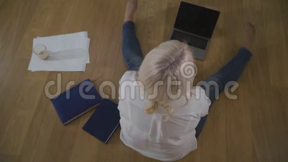 高瞻远瞩的成熟白种人女人穿着牛仔裤和白色衬衫坐在木地板上女性退休人员情况良好视频的预览图