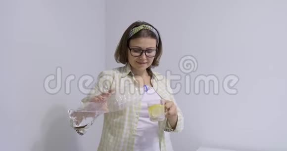 成熟的微笑女人从装有柠檬的瓶子里倒矿泉水视频的预览图