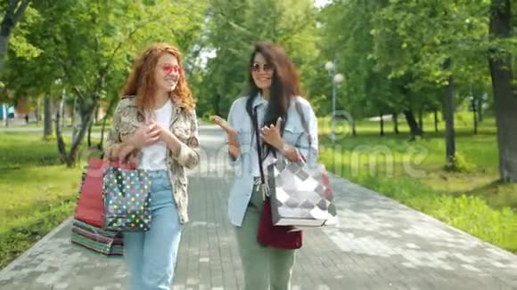 年轻女性购物狂们拿着购物袋在公园里散步视频的预览图