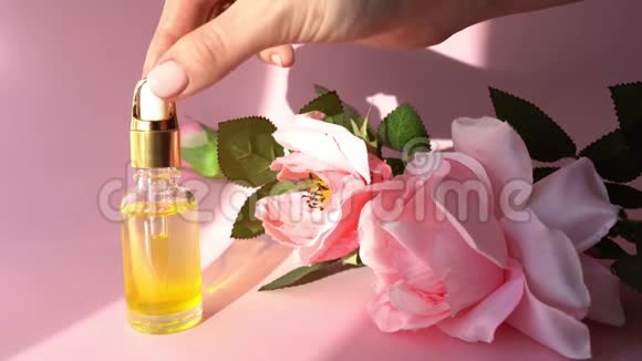 滴管玻璃瓶模型在女性手上的粉红色背景与花化妆品吸管上的油污掉落视频的预览图