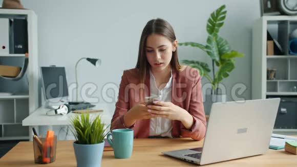 漂亮的女士用智能手机触摸屏幕微笑着坐在办公桌前视频的预览图