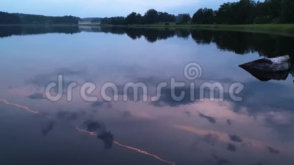 在平静的夏夜欣赏绚丽的日落湖岸有绿树和植物在晶莹洁净的镜面水中倒影视频的预览图