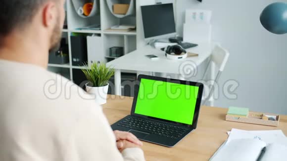 在办公桌旁的办公室里商务人员正在观看带有彩色钥匙绿色屏幕的笔记本电脑视频的预览图