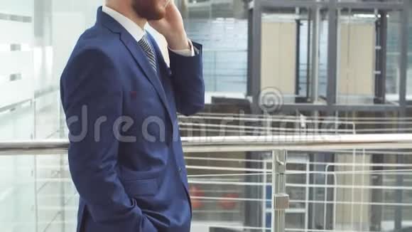 穿商务服的年轻商人用智能手机站在现代商务中心大厅视频的预览图