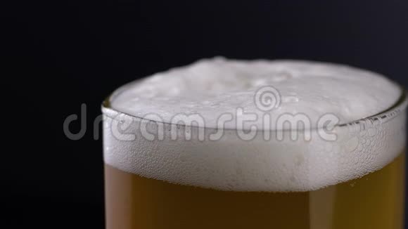 将新鲜和冷的工艺啤酒放在一个杯子里上面有白色泡沫背景是黑色的流动的泡沫小麦或视频的预览图