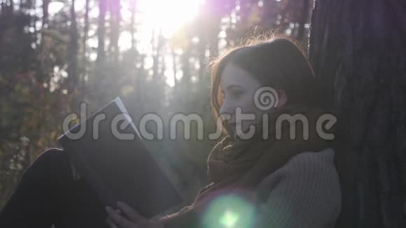 秋林年轻迷人的女人穿着舒适的衣服手里拿着书在阳光下看书视频的预览图