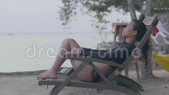 年轻女子坐在海滩的椅子上在宁静的海滩度假胜地放松视频的预览图
