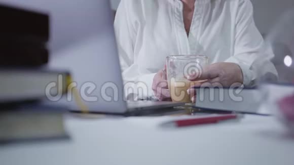 特写成熟女性手拿咖啡杯和使用笔记本电脑高加索族女性在家上网视频的预览图