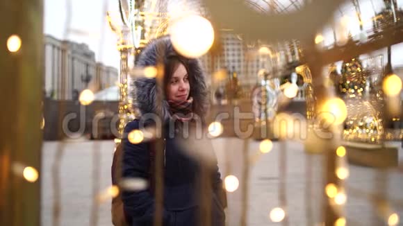 一个穿着夹克和引擎盖的漂亮年轻女人穿过街道上的花环的肖像视频的预览图