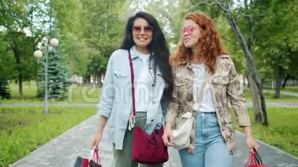 年轻女士带着购物袋在户外散步时慢动作说笑视频的预览图