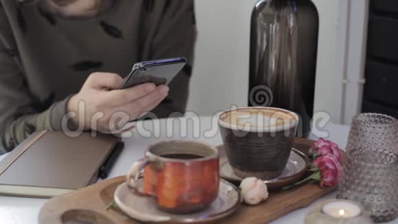 女孩手里拿着手机一边拿着咖啡坐在桌旁一边翻书页视频的预览图