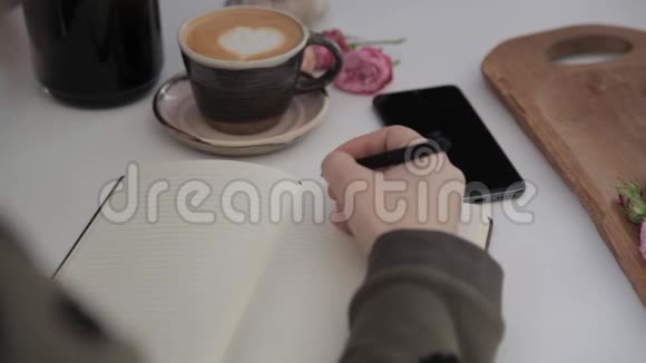 女孩的手写着我爱你写在一本笔记本上写在一张白色的桌子上旁边是一杯咖啡视频的预览图