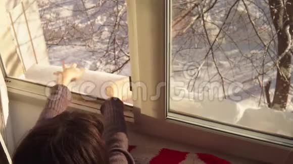 布鲁内特女孩手捧雪藏在打开的窗户后面视频的预览图