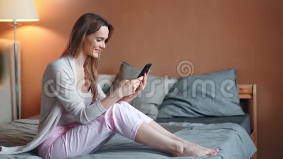 舒适的家里光着脚爱聊天的女性坐在床上放松视频的预览图