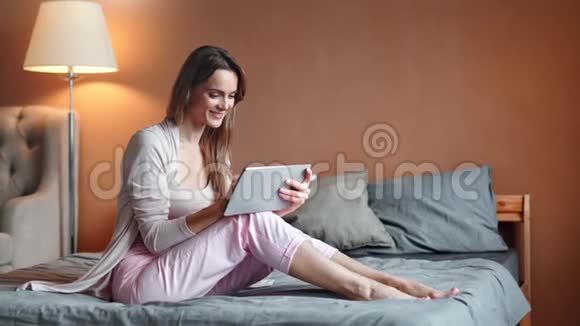 微笑年轻的家庭妇女聊天使用平板电脑坐在床上积极的情绪视频的预览图