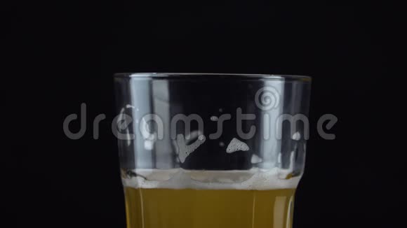 将新鲜和冷的工艺啤酒倒入一个玻璃中上面有白色泡沫在黑色背景上流动的泡沫小麦或啤酒视频的预览图