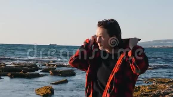 伤心的女人在海滩上变冷了孤独的女人穿着格子红色衬衫忧郁的女人看着海平线孤独寂寞视频的预览图