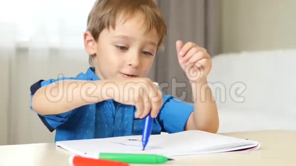 快乐的男孩坐在桌子旁有趣地画着五颜六色的钢笔孩子花时间去创造视频的预览图